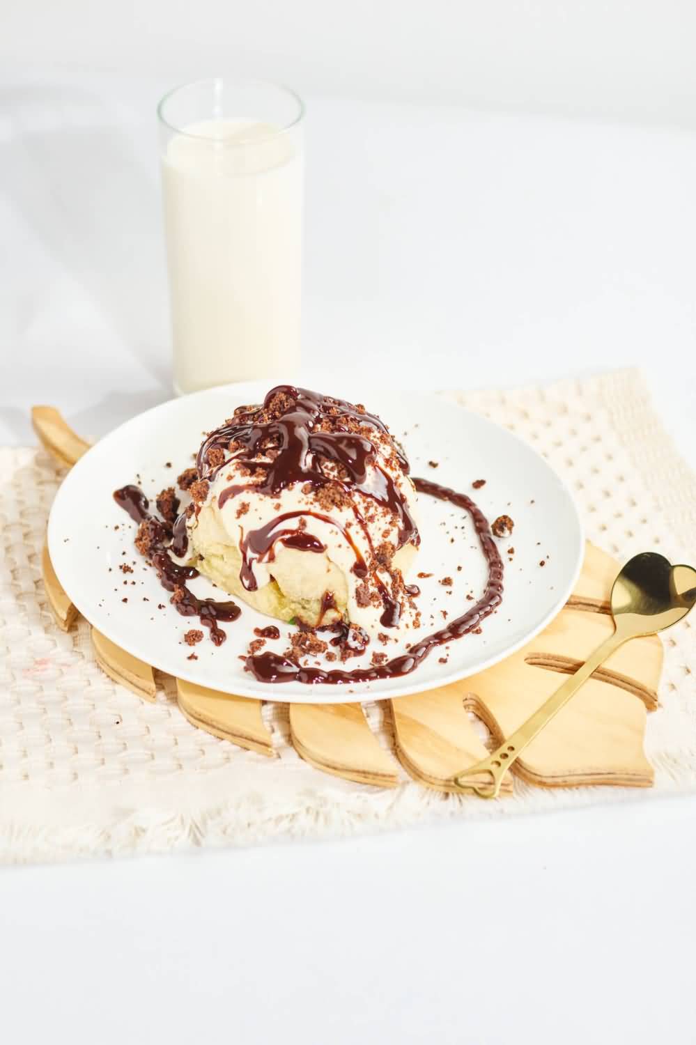 Un cinnamon roll esponjoso con un relleno de canela y nueces caramelizadas, hecho en la ciudad de Medellín, servido en un plato blanco sobre un mantel texturizado color crema, acompañado de una cuchara dorada decorativa con forma de corazón en el mango.