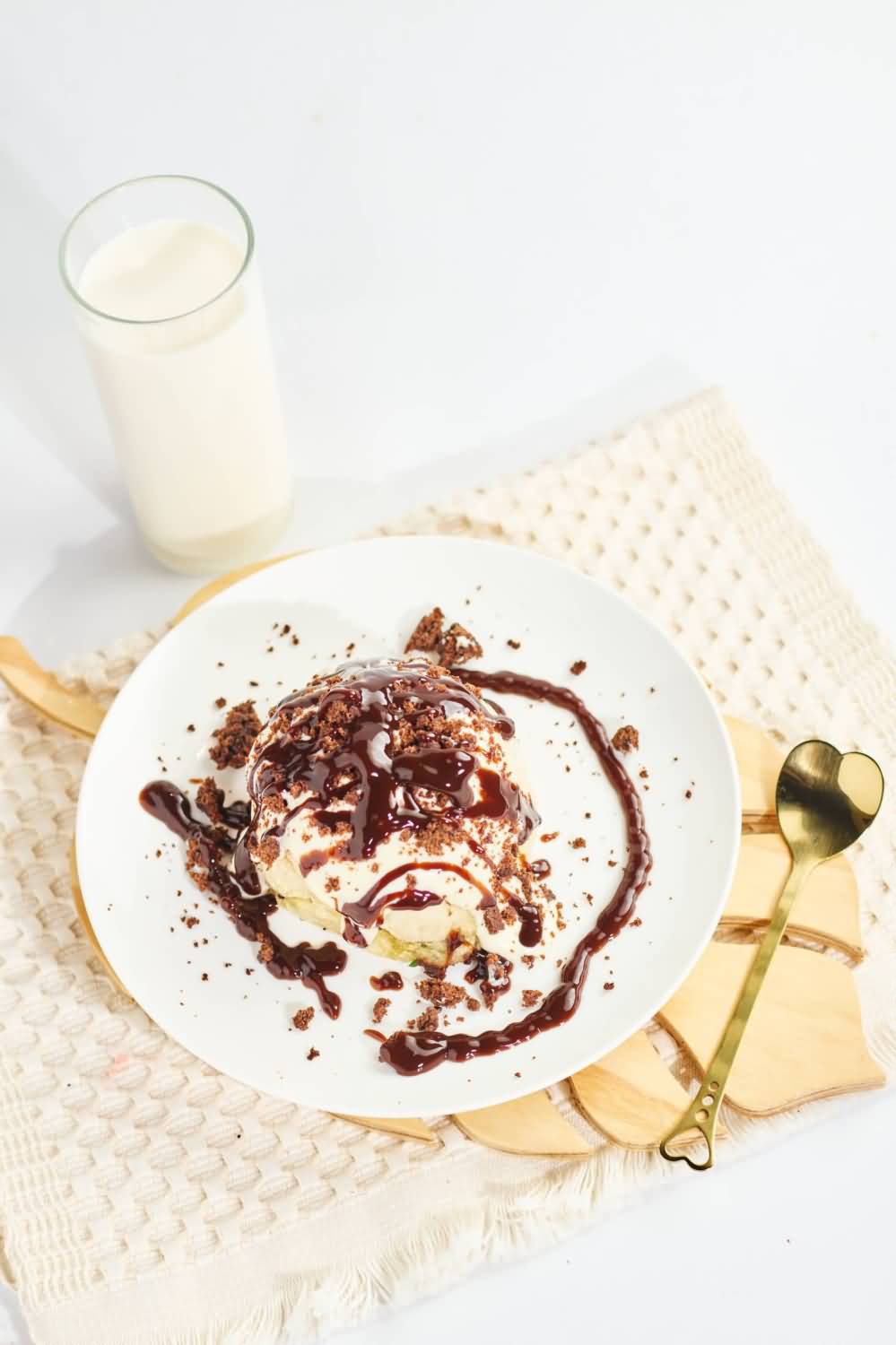 Un cinnamon roll esponjoso con un relleno de canela y nueces caramelizadas, hecho en la ciudad de Medellín, servido en un plato blanco sobre un mantel texturizado color crema, acompañado de una cuchara dorada decorativa con forma de corazón en el mango.