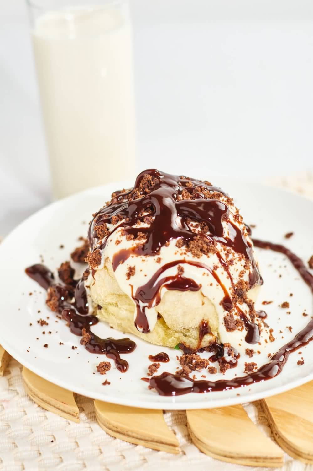 Un cinnamon roll esponjoso con un relleno de canela y nueces caramelizadas, hecho en la ciudad de Medellín, servido en un plato blanco sobre un mantel texturizado color crema, acompañado de una cuchara dorada decorativa con forma de corazón en el mango.